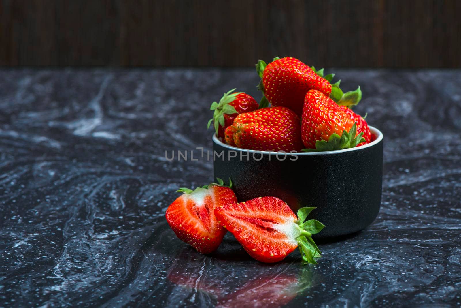 Strawberries on black marble. Ripe strawberries in a saucer on a black background. Place to insert text.