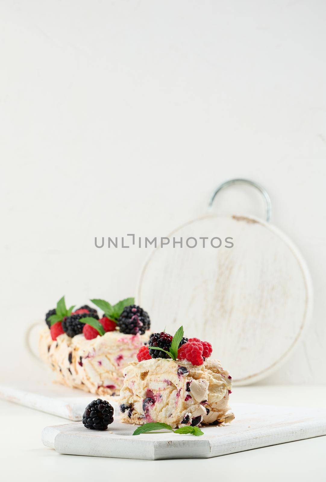 Baked meringue roll with cream and fresh fruits on a white wooden board, delicious dessert