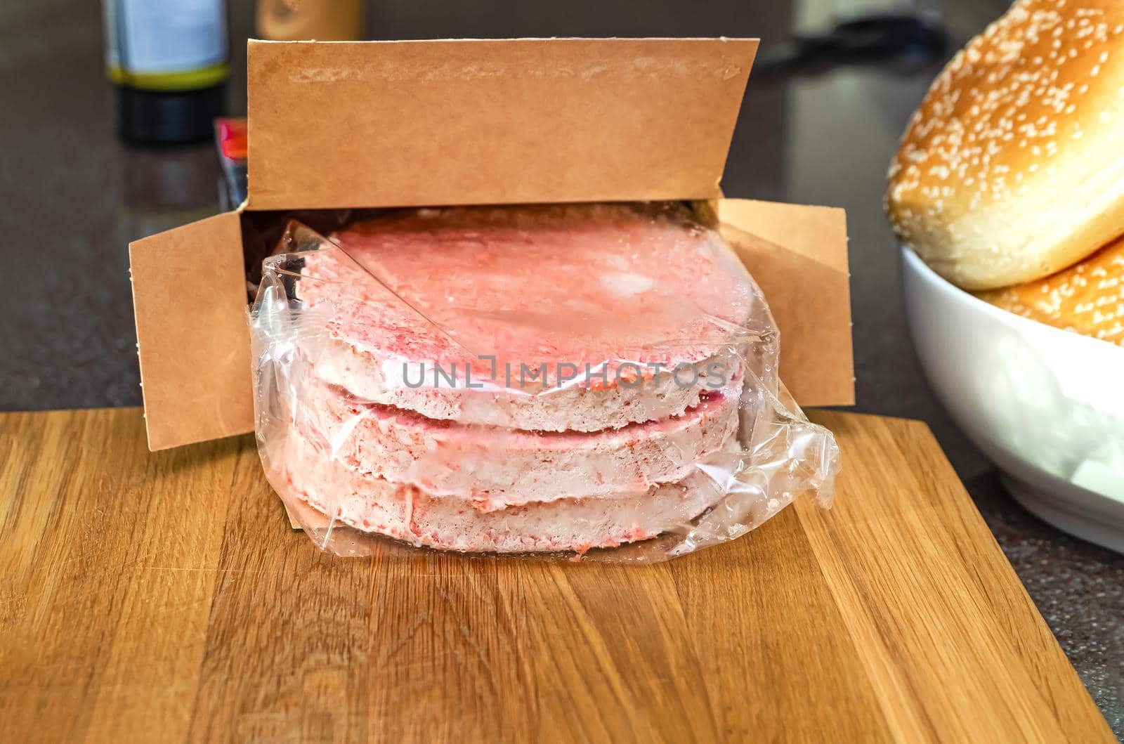 Defrost wrapped frozen burger meat before cooking. On a wooden cutting board on the kitchen table.