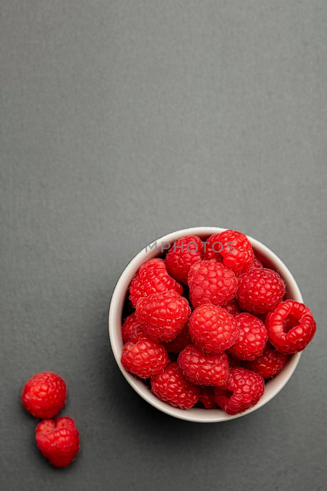 Fresh juicy raspberries in a small black plate. Bright red crimson close-up. Summer berry picking time. Healthy organic fruits for kids. Vertical photo by SERSOL