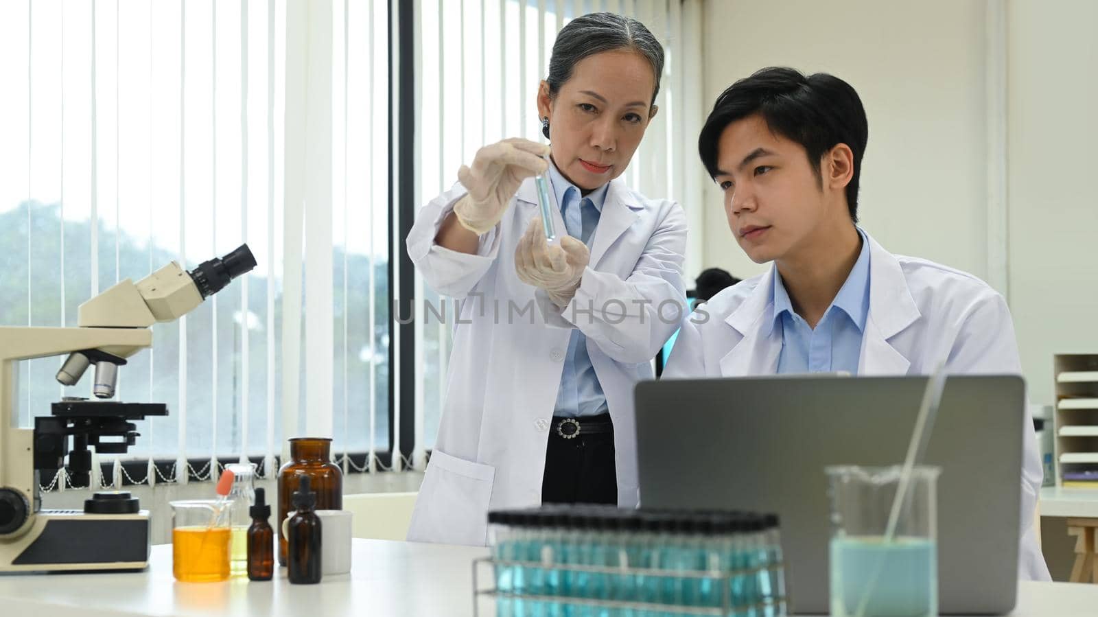 Young man and senior female biotechnology specialist supervisor conducting experiment in a laboratory.
