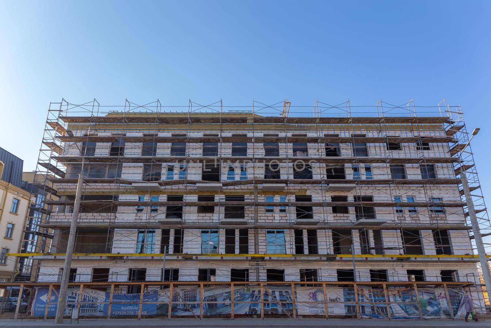 Insulation of the exterior walls of a building under construction. The walls of the building under construction are surrounded by scaffolding for workers to access. Exterior finishing works.