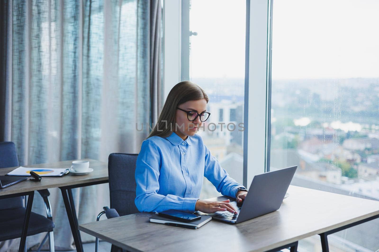 Young beautiful business woman in a blue shirt sitting in the office with a laptop and doing business