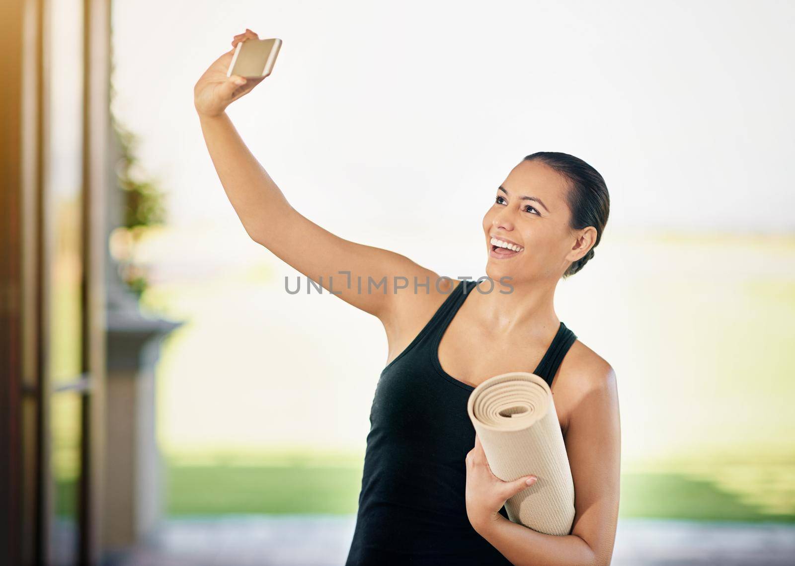 Yoga selfie. a young woman taking a selfie while carrying her yoga mat