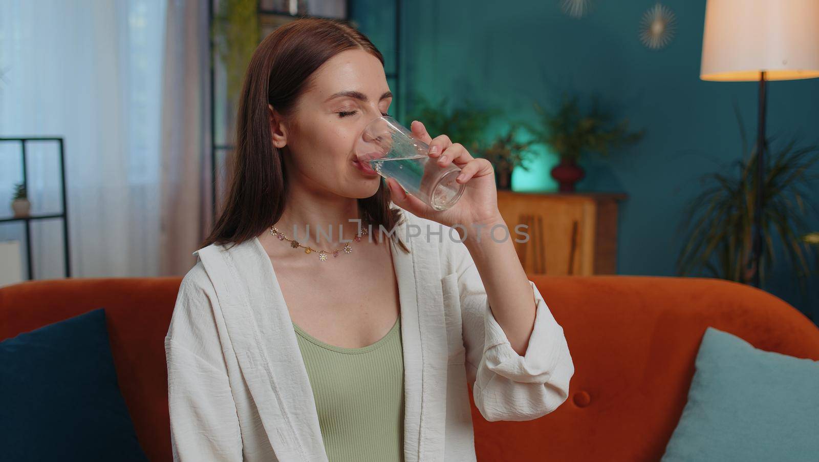 Portrait of thirsty lovely girl sitting indoors holding glass of natural aqua make sips drinking still water preventing dehydration. Woman with good life habits, healthy slimming, weight loss concept