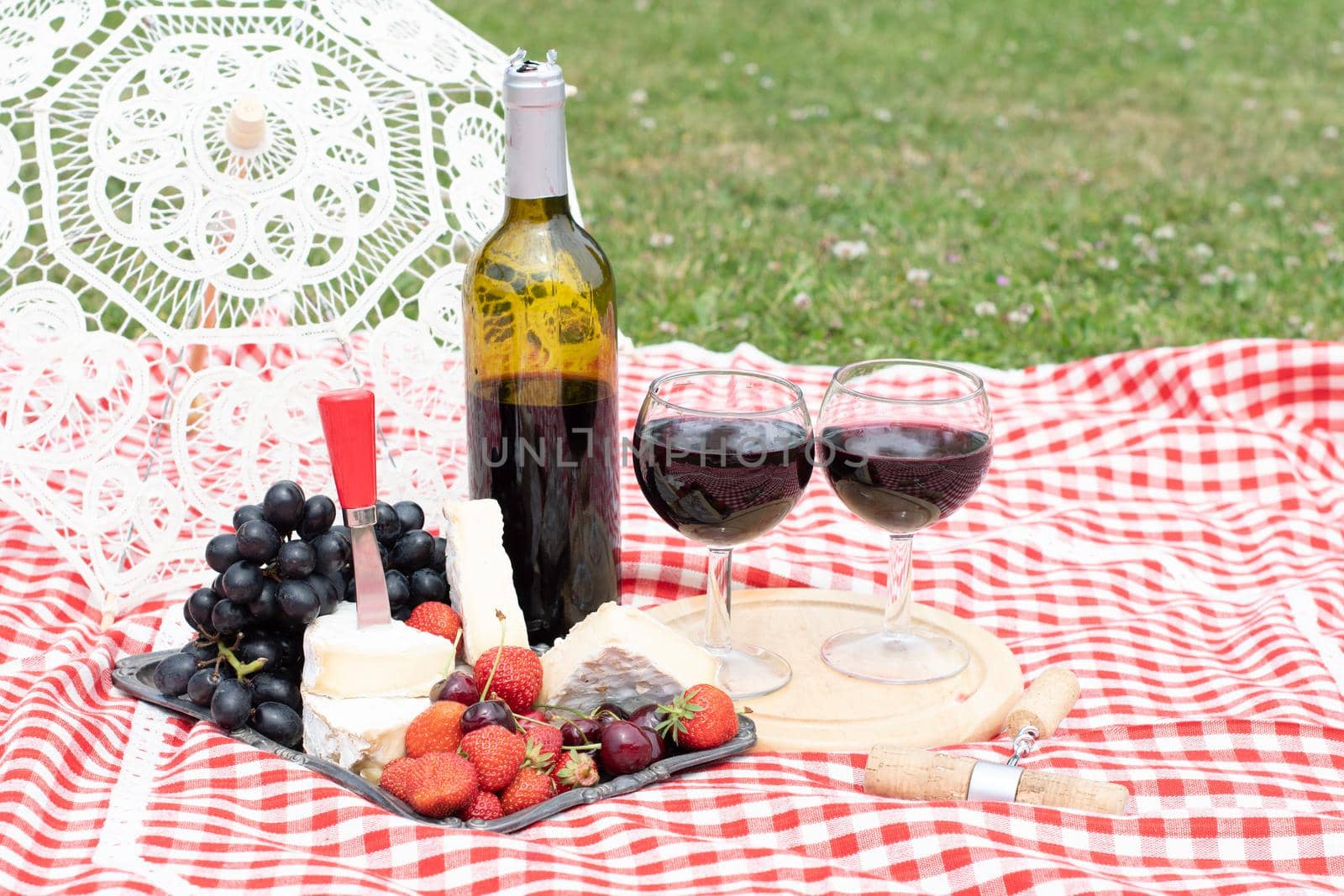 summer picnic on a green lawn with red wine, cheese and fresh berries, grapes, cherries, strawberries, summer vacation. High quality photo