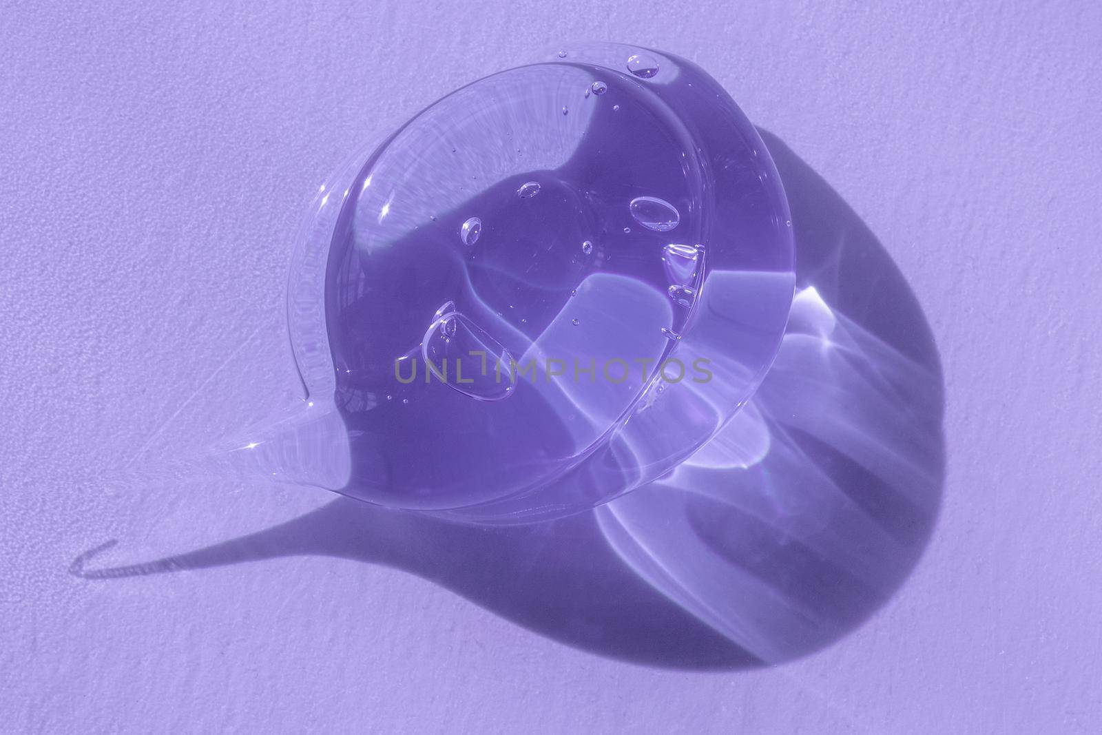 Glycerin or gel smear smudge swatch on lilac backdrop with shadow. Cosmetic product closeup texture with tiny bubbles. Styling gel lotion, cleanser, transparent shampoo drop.. by photolime