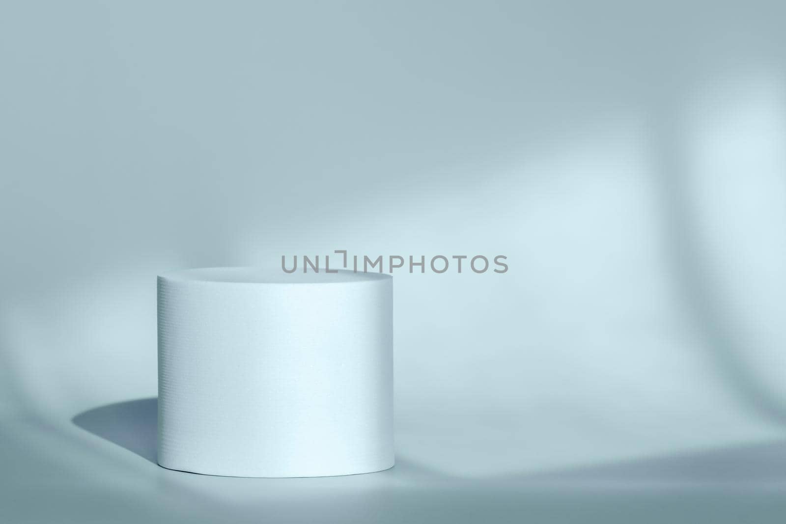 Blue round pedestal podium for packaging presentation on backdrop with room shadows from window. Circle platform stage for cosmetic products with geometric shadow on wall. Minimalist style