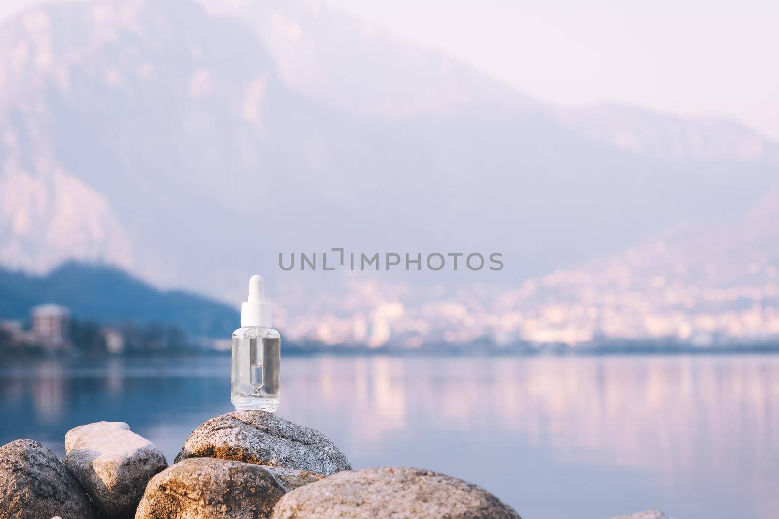 Hyaluronic acid, serum skincare glass bottle on stone, mountain lake background. Serum product cosmetic with peptide and collagen. Modern brand cosmetics packaging with shadow. by photolime