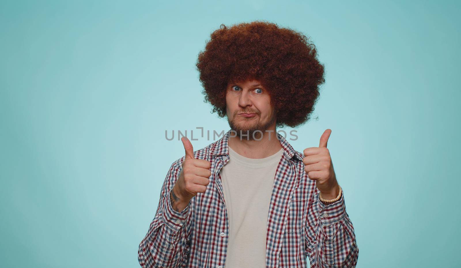 Great job, nice. Cheerful positive happy bearded man in shirt showing thumbs up and nodding in approval, successful good work. Young stylish one guy on blue studio background. People sincere emotions