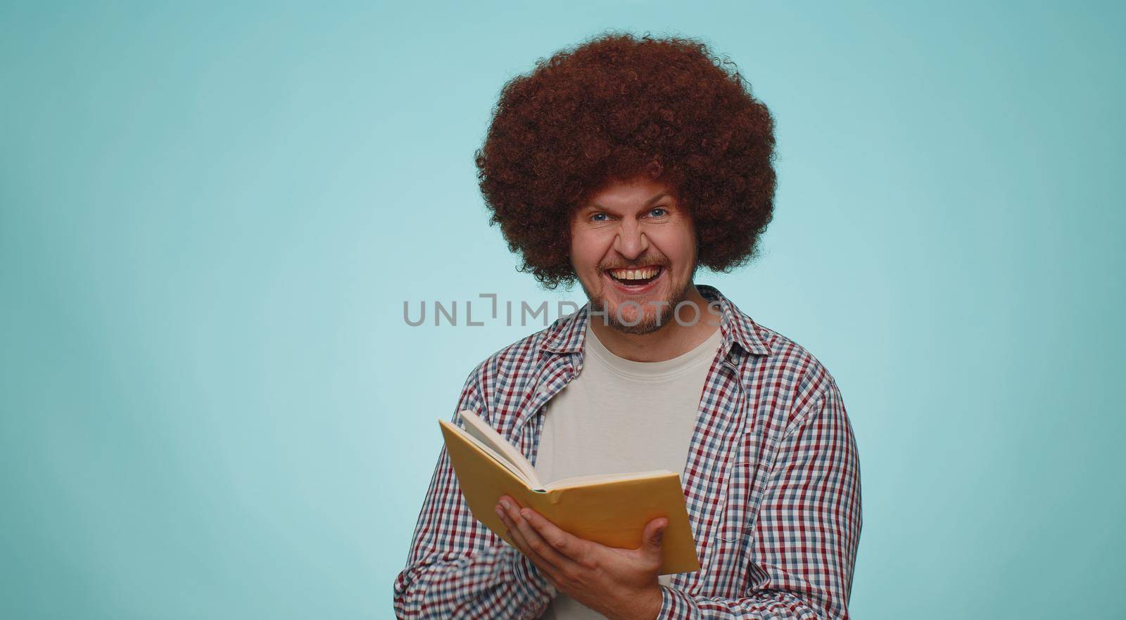 Happy smiling bearded man reading funny interesting fairytale story book, leisure hobby, knowledge wisdom, education, learning, study, wow. Young adult guy boy isolated alone on blue studio background