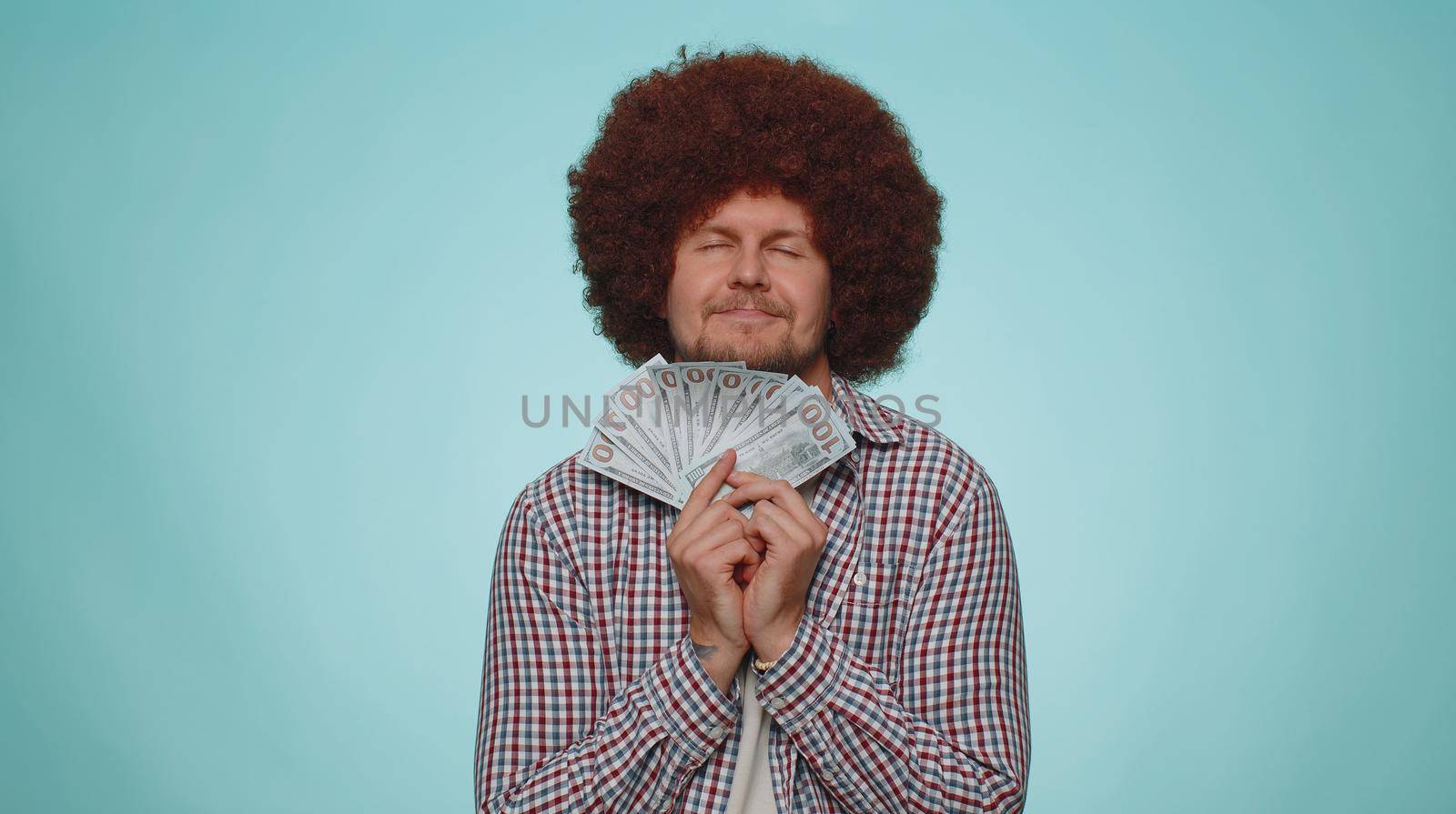 Rich pleased boss bearded man waving money dollar cash banknotes bills like a fan, success business career, lottery winner, big income, wealth. Young guy boy isolated alone on blue studio background