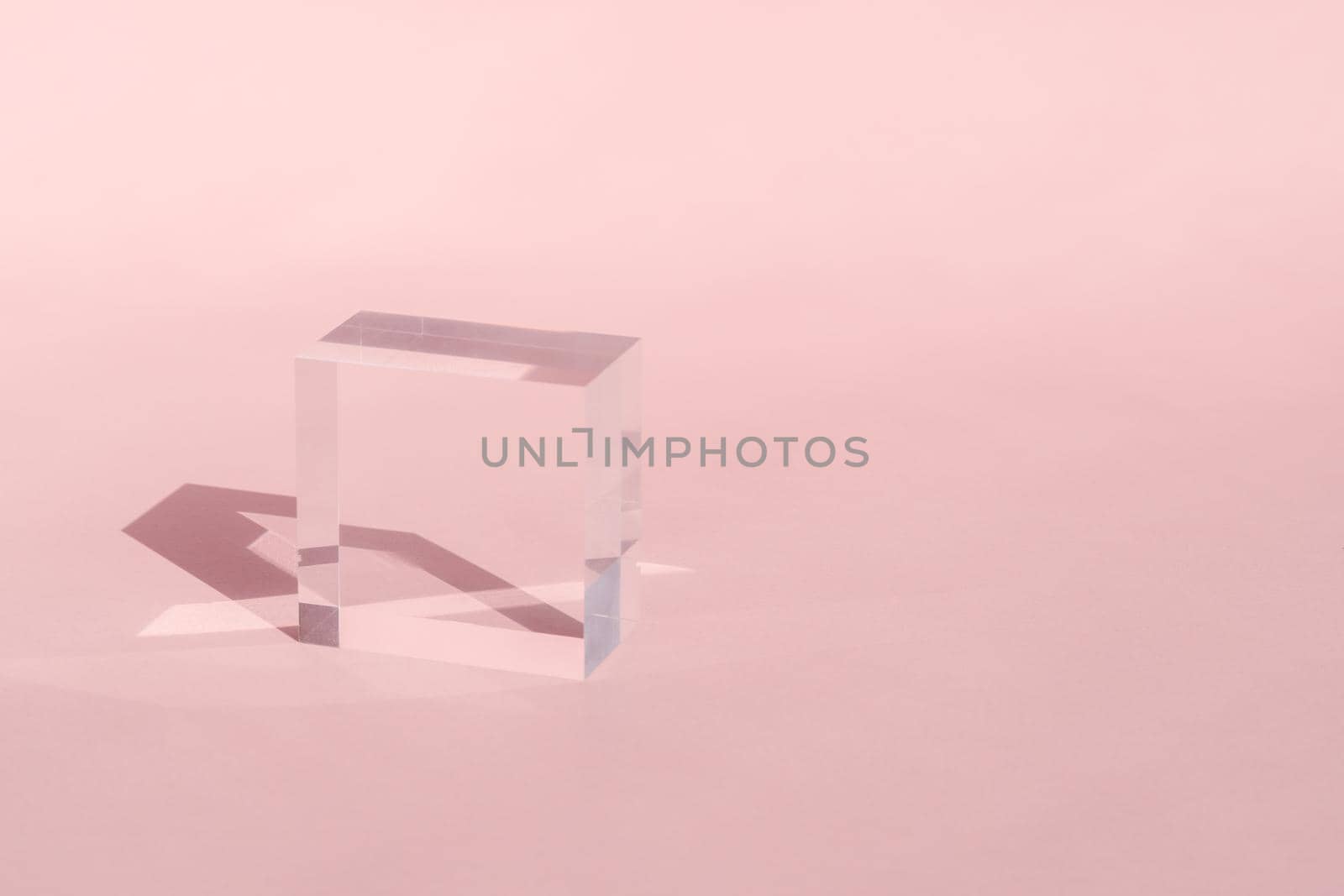 Acrylic block, podium for product presentation. Glass transparent cube with sun reflection, geometric stand for cosmetic, light and shadow on pink. Physics refraction effect by photolime