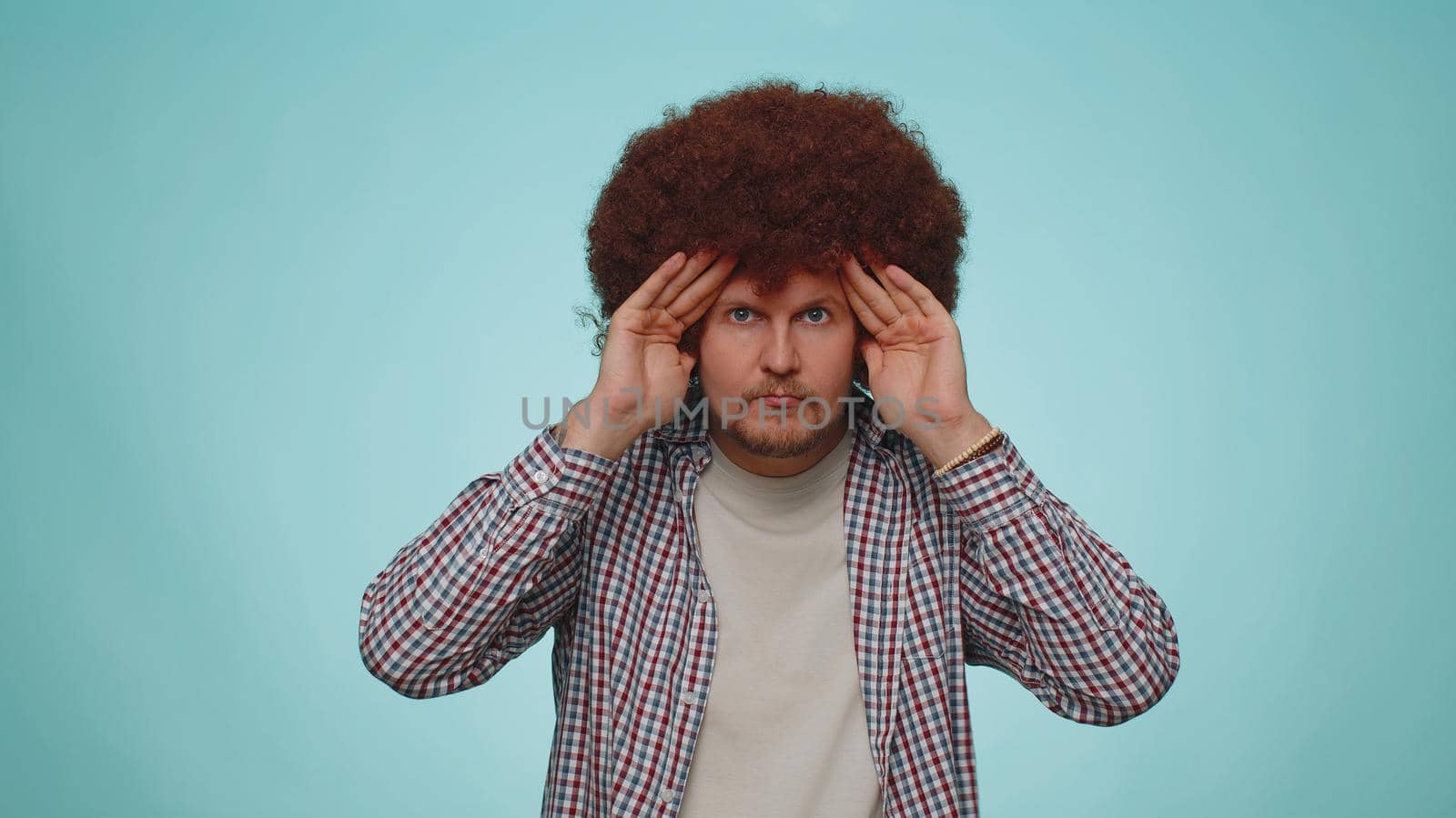 Nosy curious man closing eyes with hand and spying through fingers, hiding and peeping, binocular gesture, exploring way, seeking something in distance. Young adult guy boy on blue studio background