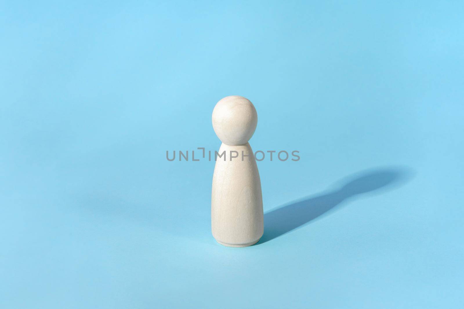 Abstract concept of lonely person. Minimalist, wooden figure with shadow on blue by photolime