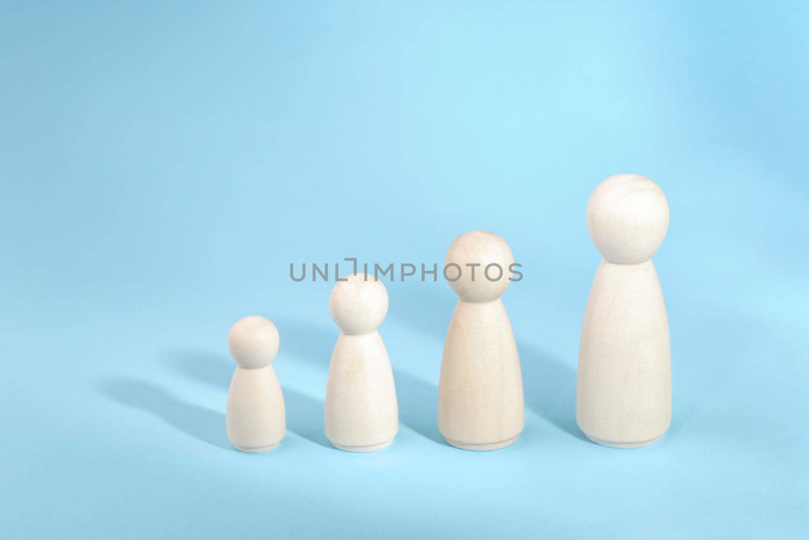 Wooden figurines standing in a row from low to high. Person growth on blue background. by photolime