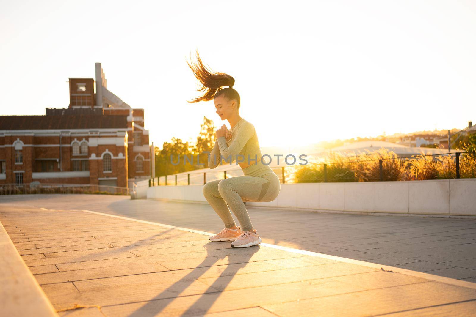 Sporty woman doing jumping squats exercises on stairs in park. Bodyweight training on sunset. Young adult fitness woman exercising outdoor. European woman squats. Athletic caucasian female workout