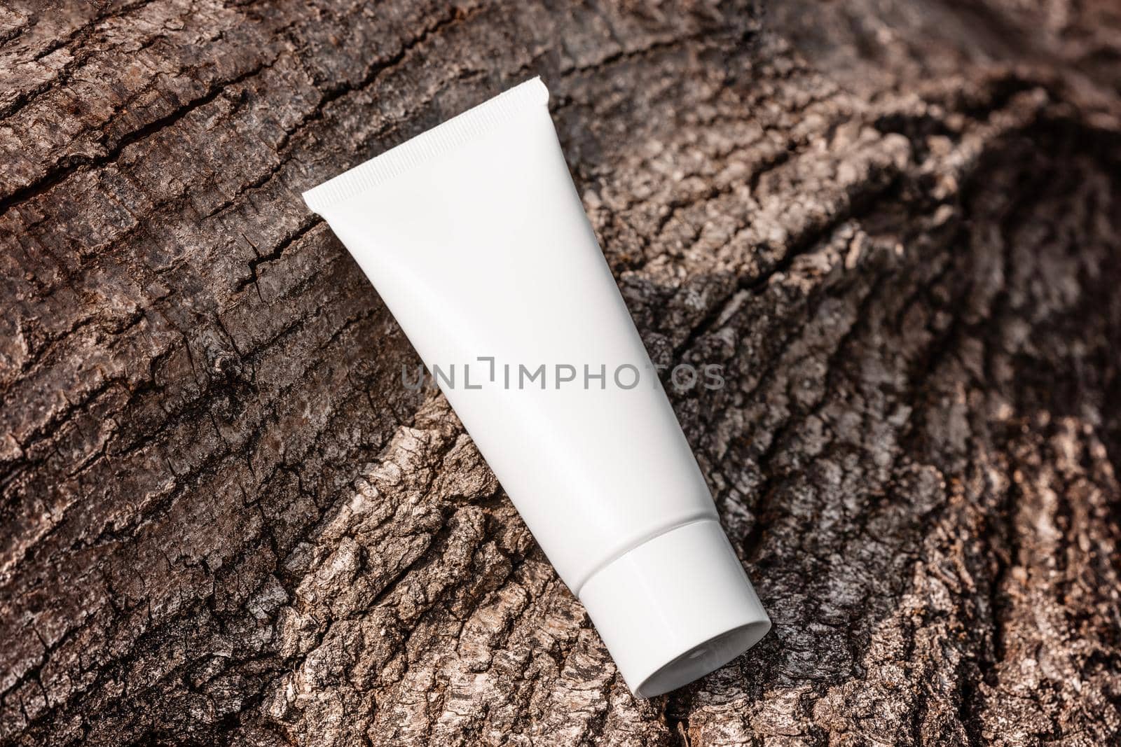 Hand cream, moisturizer, lotion in white plastic tube on tree bark top view. Anti-age product template, luxury body care. Cosmetics packaging with natural ingredients by photolime