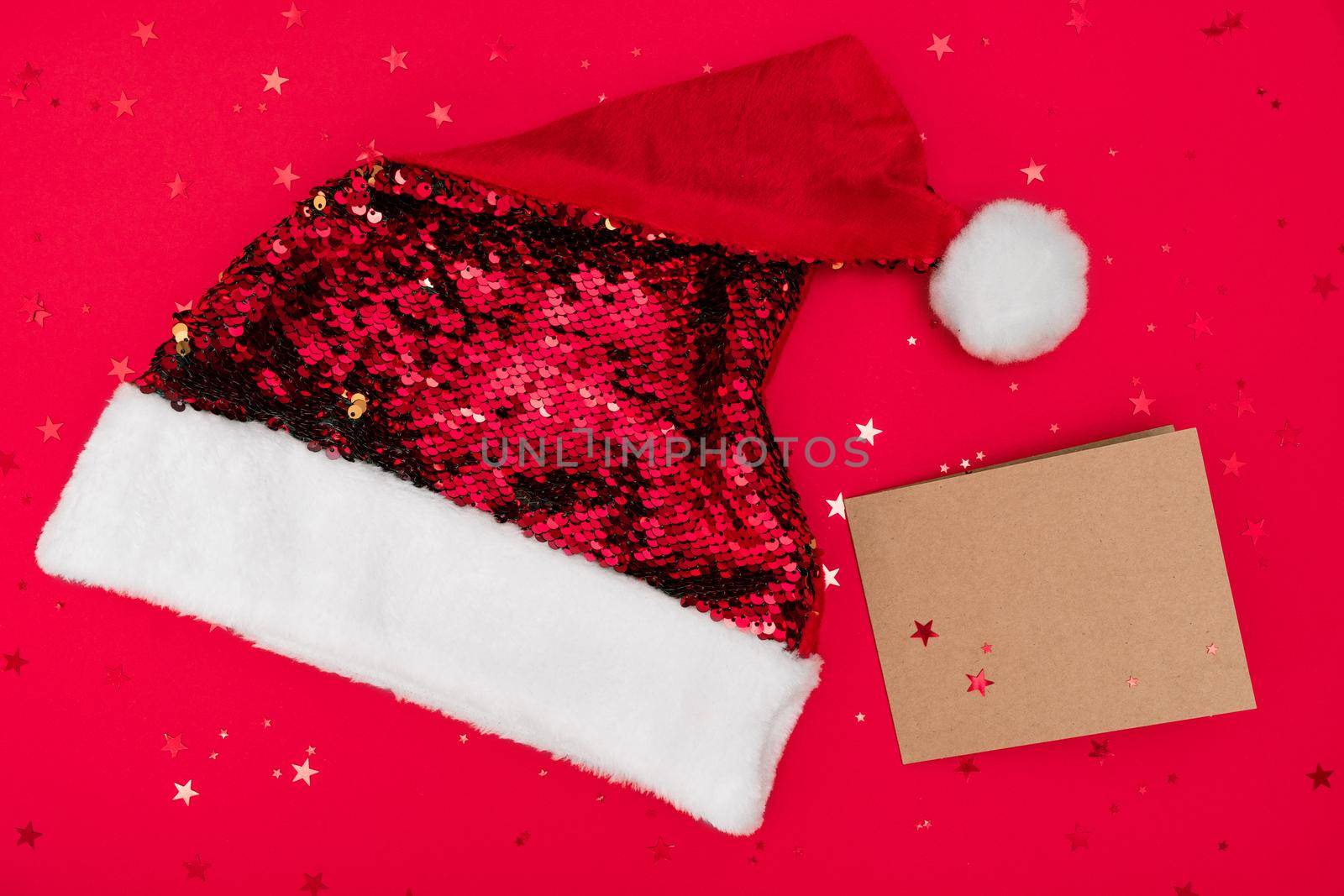 Santa red hat and postcard mock up on red background with confetti top view by photolime