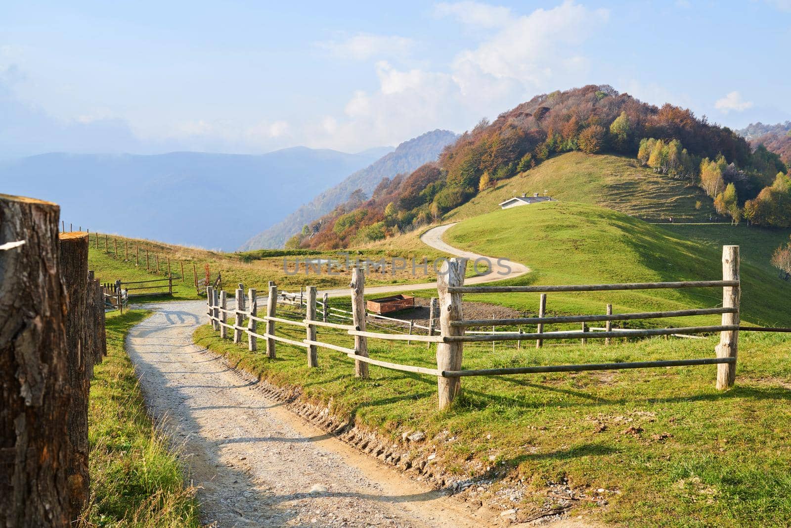 Picturesque Alps autumn landscape, wooden fence and mountain hills in Lombardy, Italy. Tourist adventure by photolime