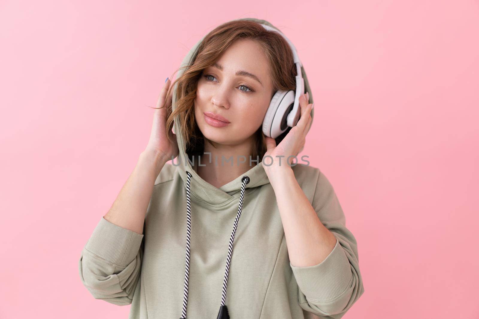 Confident woman listen music headphones Caucasian female enjoy podcast or audio books dressed oversize hoodie pink background close up portrait