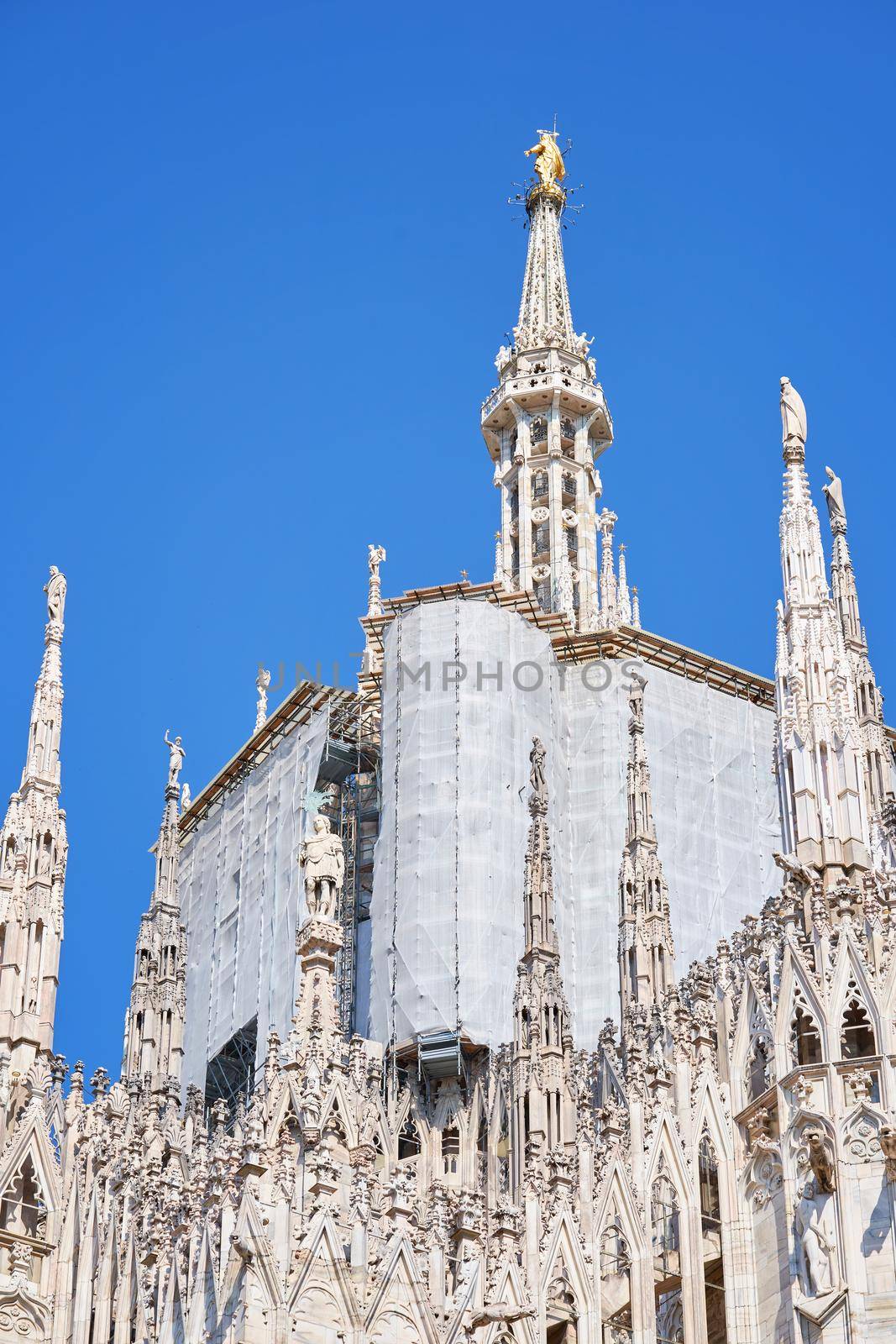 View from the bottom of Duomo cathedral building during reconstruction process with multiple metal scaffolding mounted to facade, building facade renovation. Milan, Italy