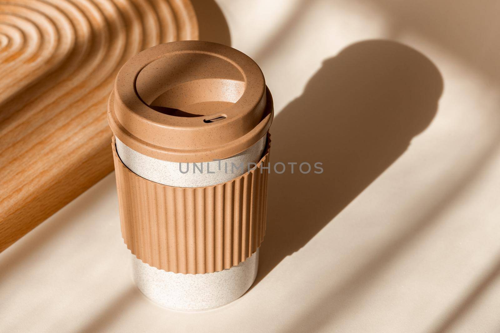 Reusable cup, biodegradable travel plastic coffee mug for take away. Sustainable bamboo eco friendly cup on natural shadow beige background. Zero waste, sustainability concept by photolime