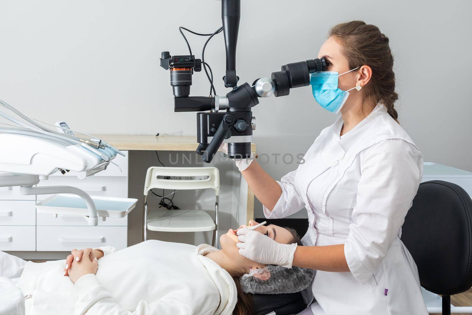 Female dentist using dental microscope treating patient teeth at dental clinic office. Medicine, dentistry and health care concept