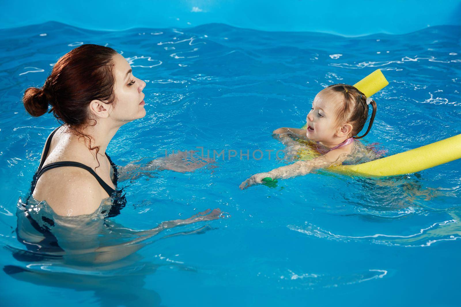 Preschool girllearning to swim in pool with foam noodle with young trainer by Mariakray
