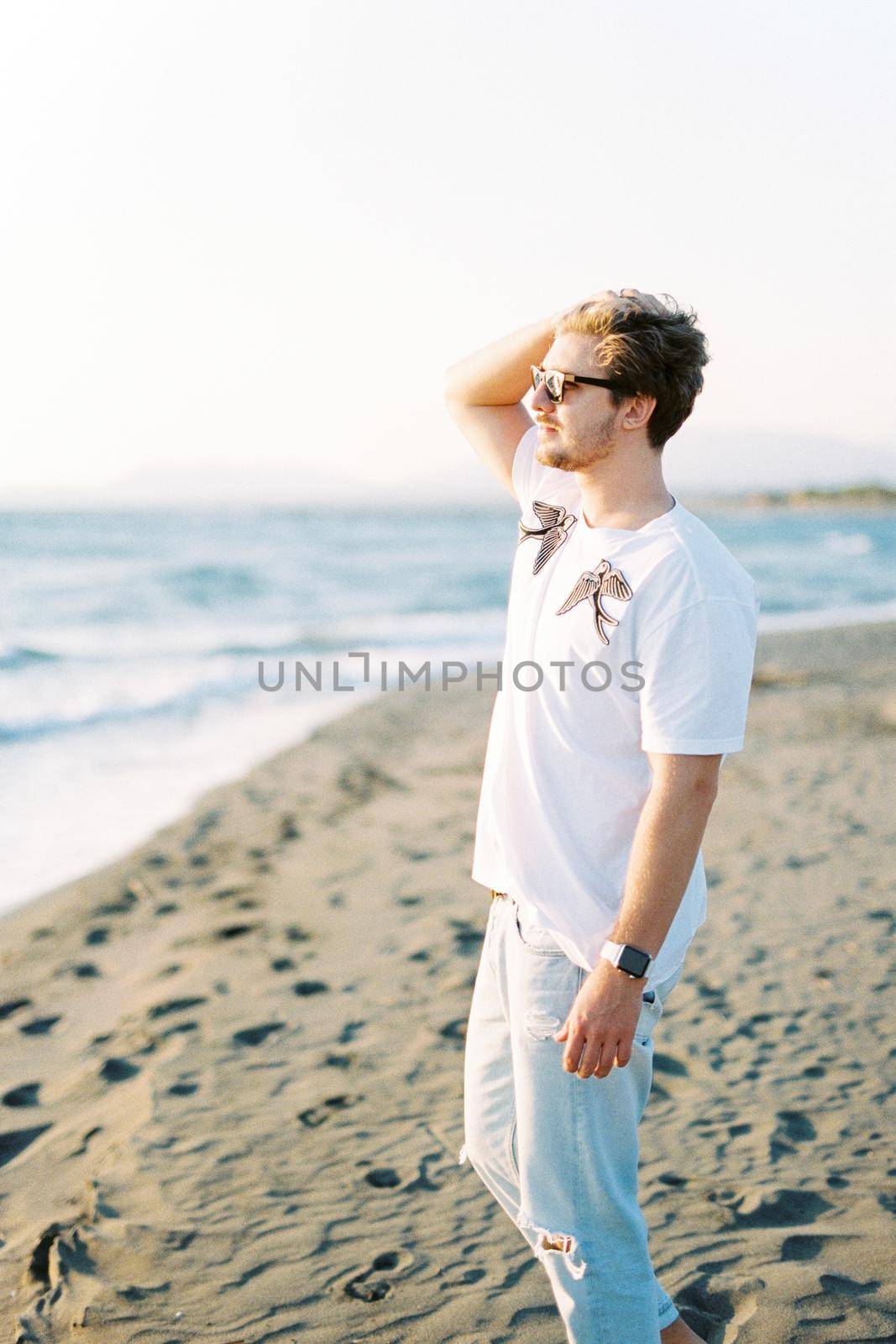 Man in sunglasses stands on the beach straightening his hair in the wind. High quality photo