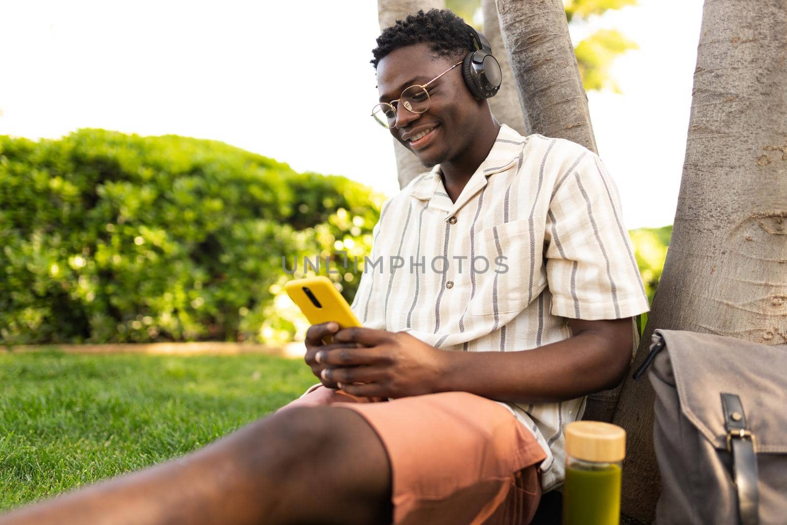 African american man relaxing outdoors listening to music using phone and headphones Black teen college student relaxing on campus. Copy space. Leisure concept.