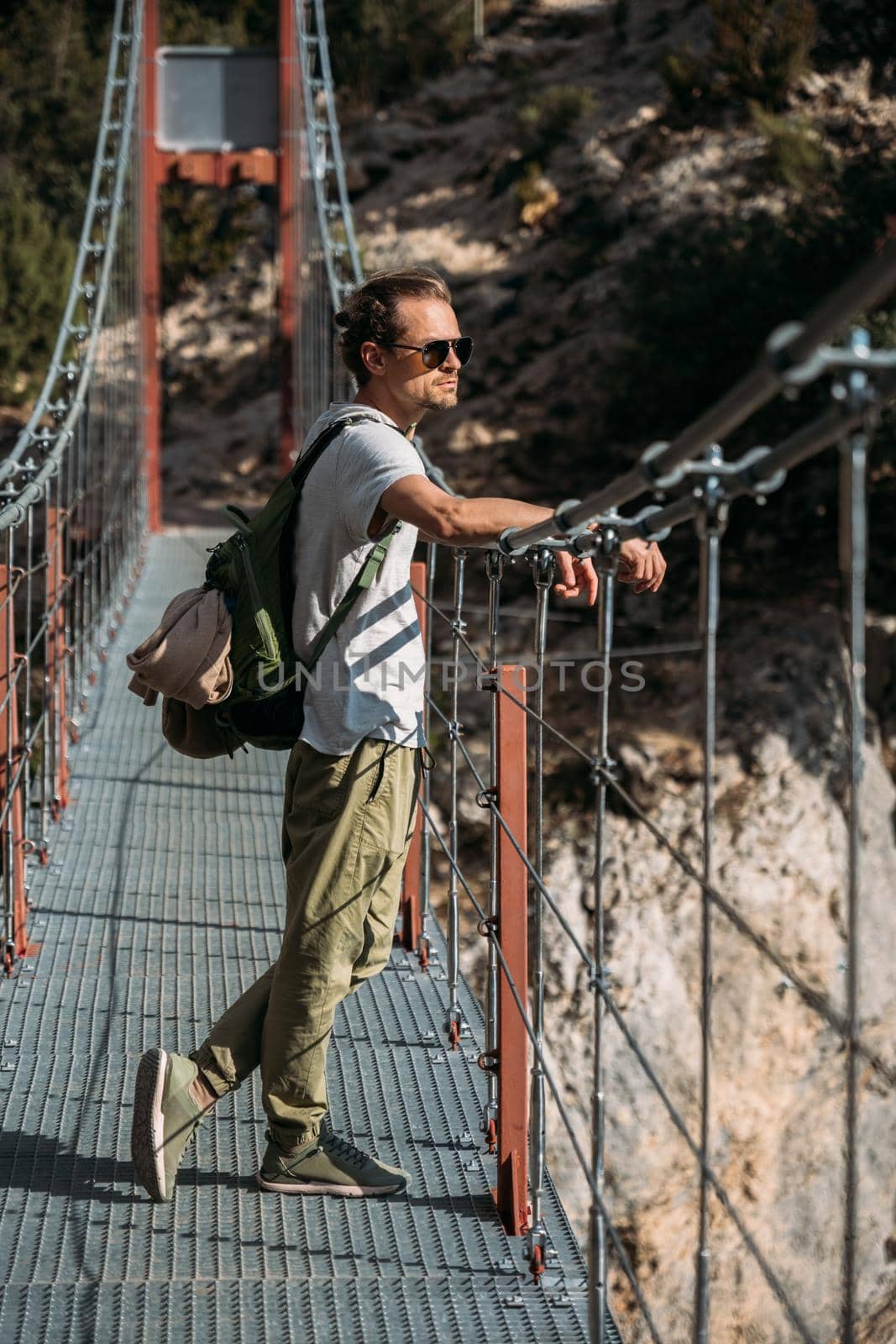 Handsome man with backpack standing on hanging bridge on a good sunny day over the lake. Travel concept by apavlin