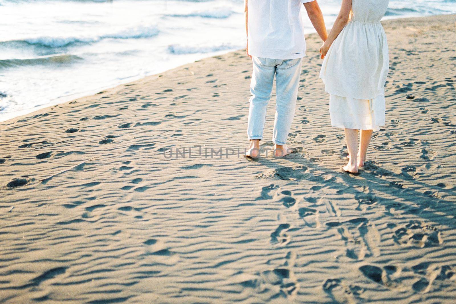 Man and woman stand on the sand holding hands. Cropped. High quality photo