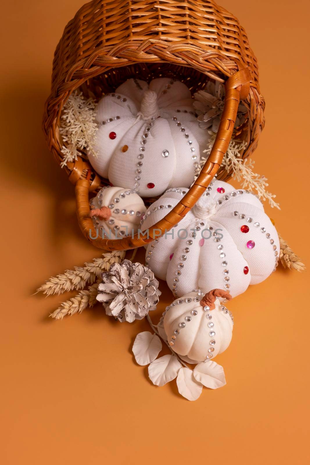 White decorative hand made pumpkins with shiny stones and pine cones in basket on colored background. Thanksgiving day by ssvimaliss