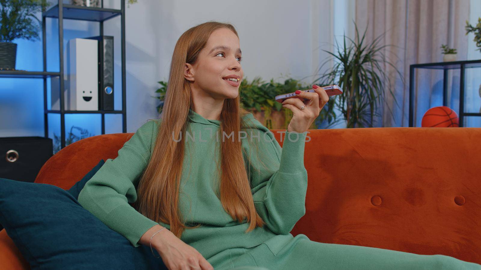 Portrait of caucasian girl making phone conversation with friends sitting call on couch at home in room. Happy excited young child kid enjoying mobile loudspeaker talking indoors at home apartment