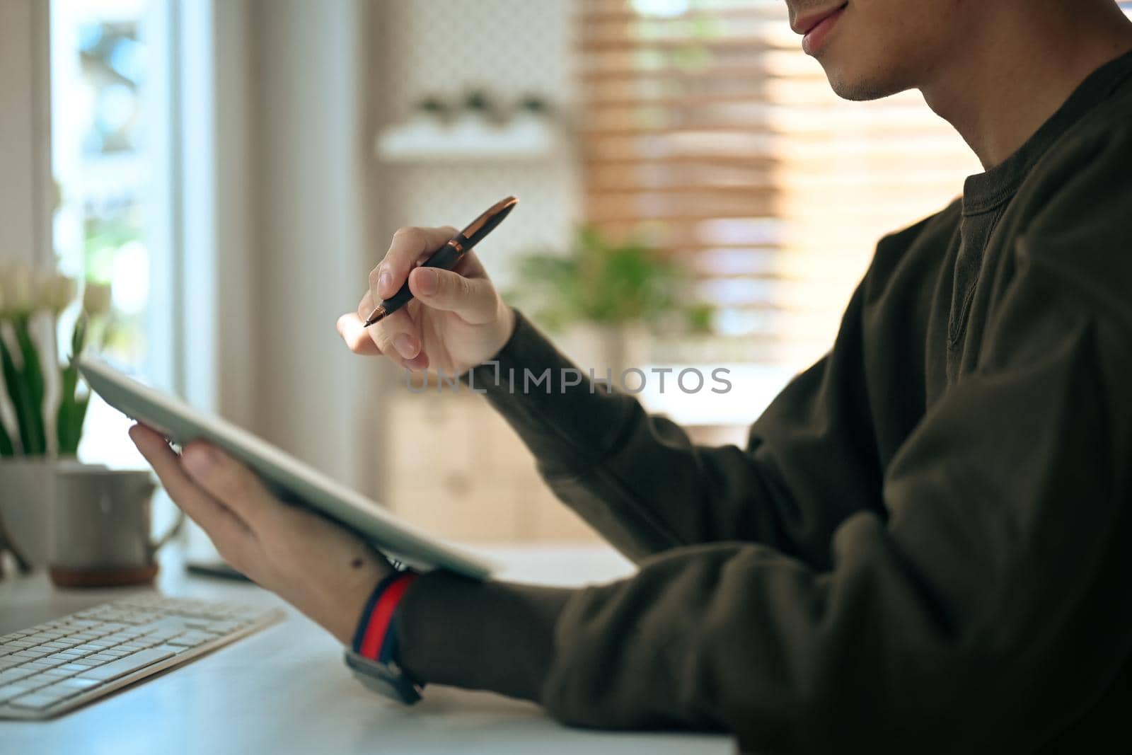 Man freelancer holding pen and using digital tablet while working online from home by prathanchorruangsak