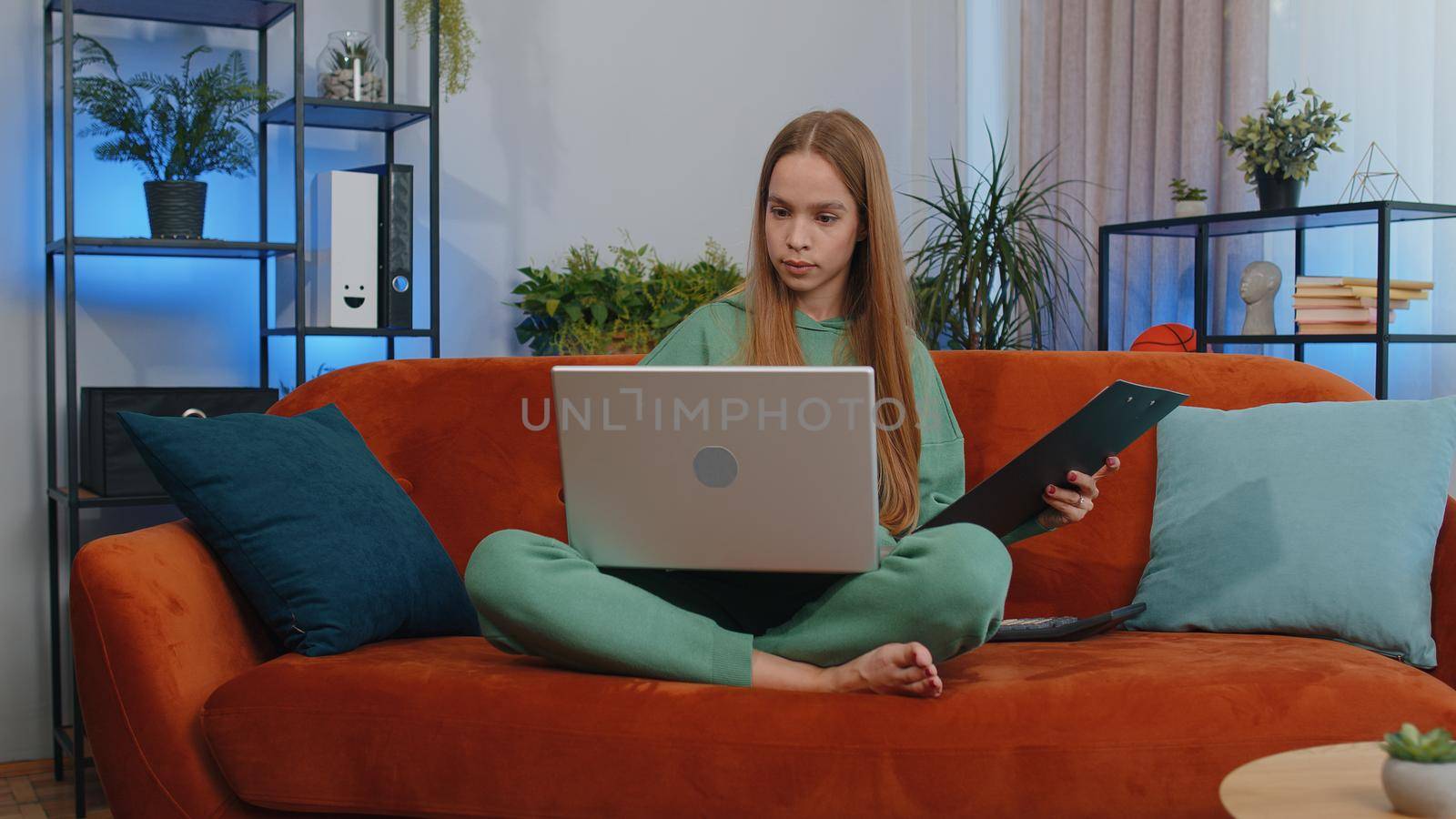 Girl accountant working with financial graph documents, calculate taxes for charts and graph reports of home income on couch. Young businesswoman working on laptop computer, planning expenses budget