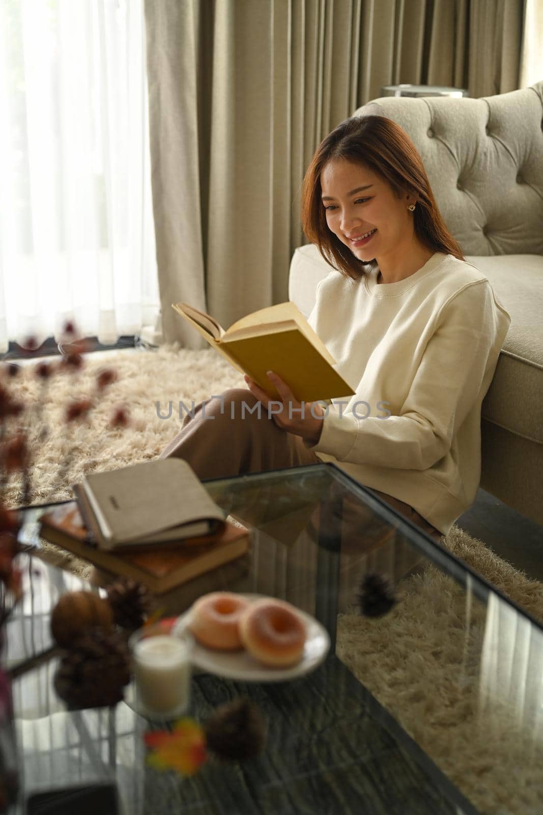Happy young woman wearing warm sweater relaxing in cozy living rom and reading book. Winter, coziness, leisure and people concept.