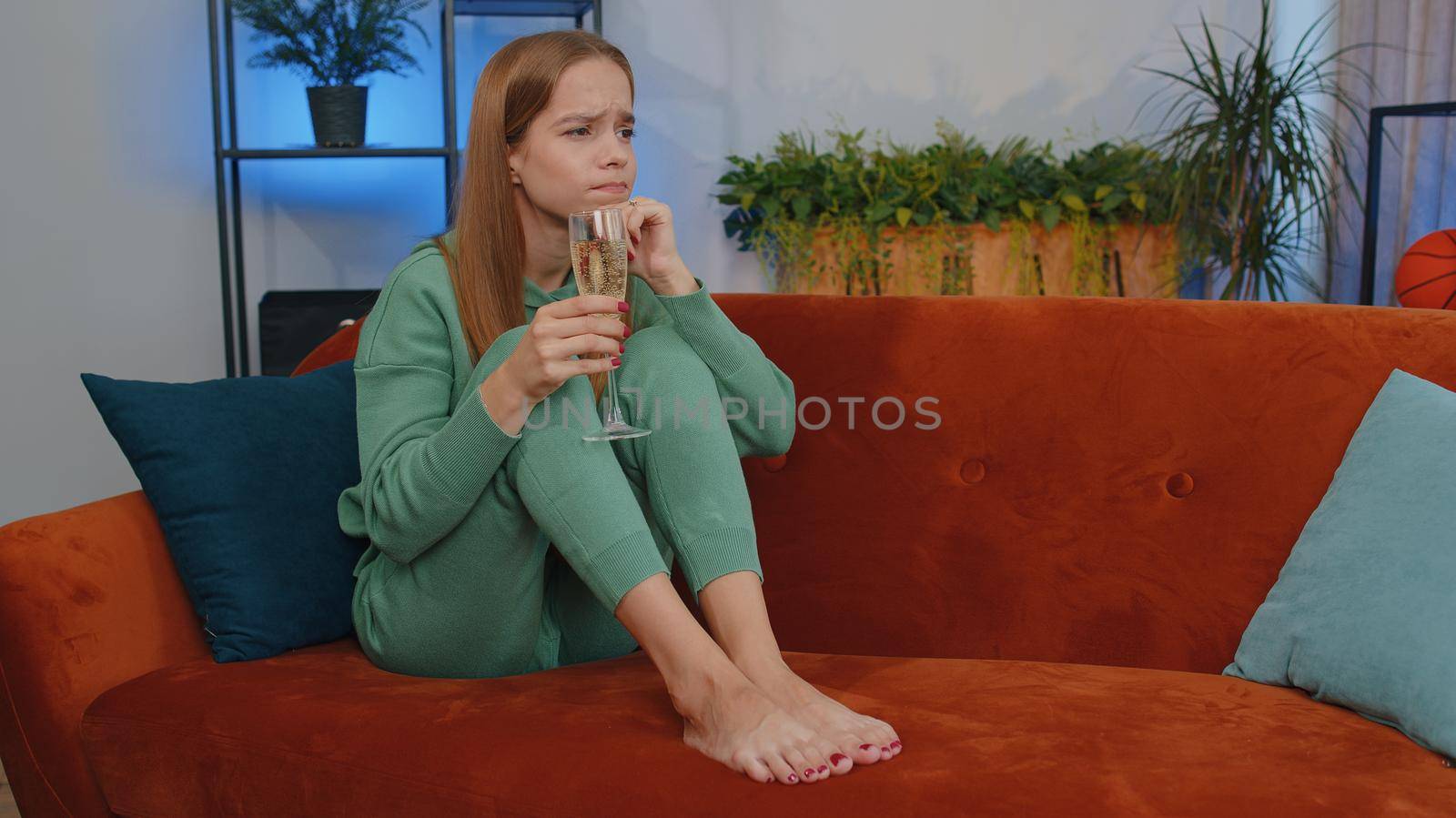 Sad young child kid looks pensive of unrequited love, suffers from unfair situation, drinking champagne. Problem, break up, depressed feeling bad annoyed, burnout, bankruptcy. Girl sits at home room