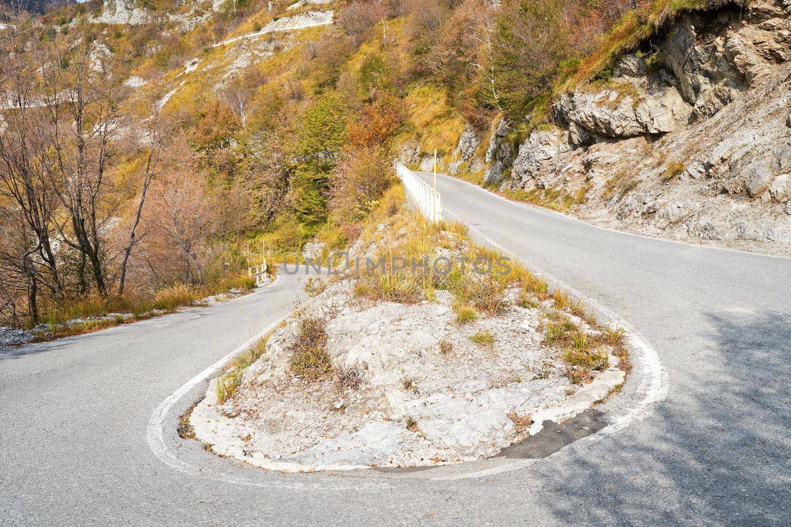 Danger curve on serpentine mountain road, picturesque Alps autumn landscape. Lombardy, Italy. by photolime