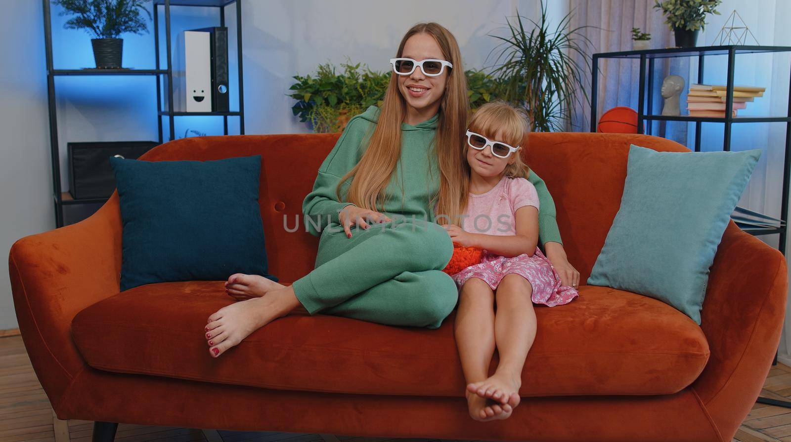 Girls friends siblings watching favorite tv show movie and eating popcorn, sitting on sofa. Female children kids family having fun laughing, relaxing, watch television online stream at home on couch