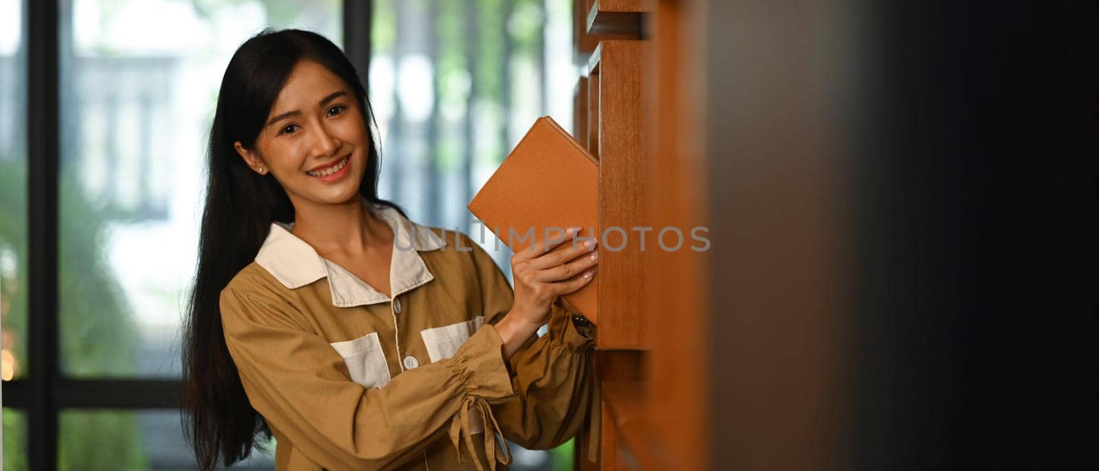 Asian female student picking up a book, choosing books from shelf in college library. Copy space for your text by prathanchorruangsak