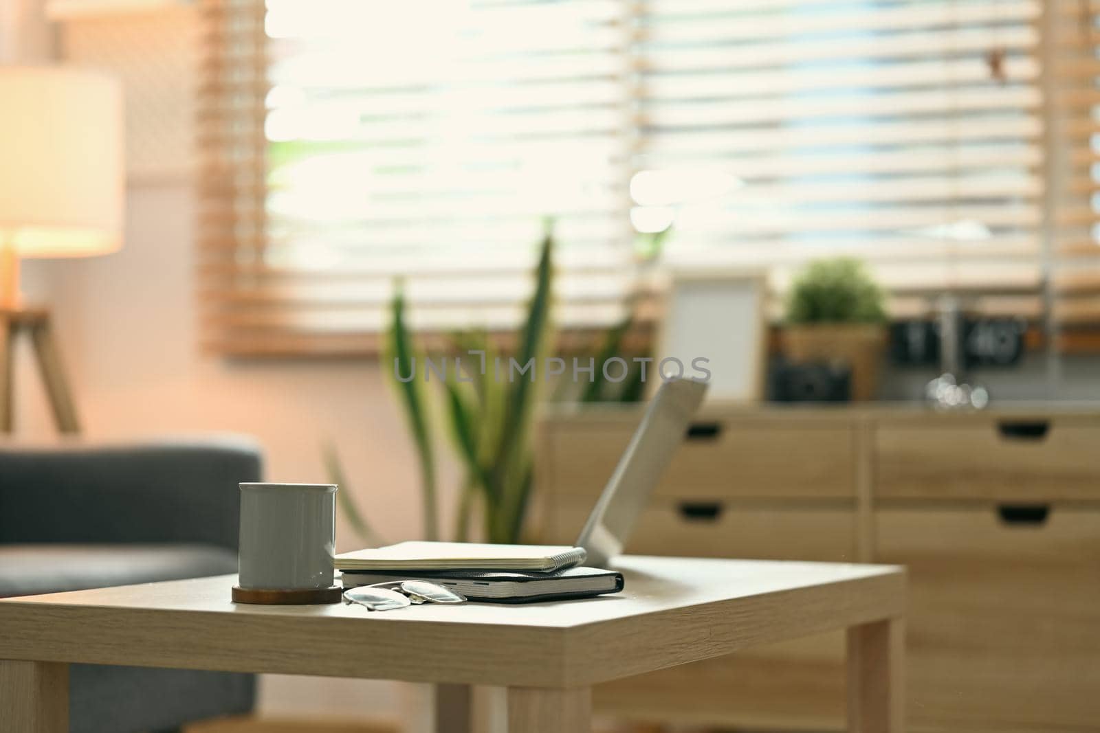 Laptop, cup of coffee and books on wooden table in comfortable living room.