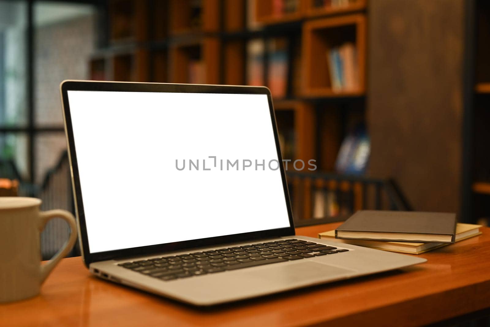Laptop computer with white empty screen, coffee cup and supplies on wooden table in contemporary office.