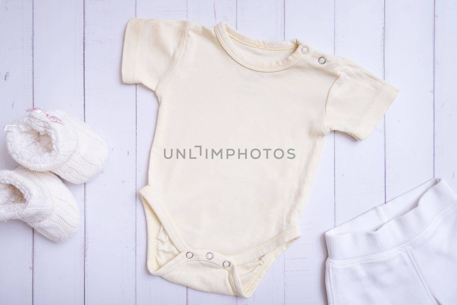 Yellow baby bodysuit mockup for logo, text or design on wooden background top view. by ssvimaliss