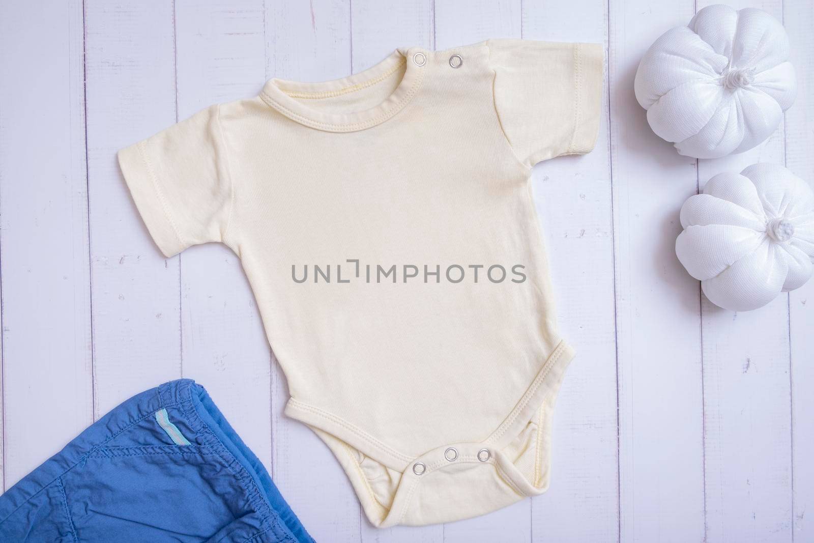 Yellow baby bodysuit mockup for logo, text or design on wooden background with pumpkins top view by ssvimaliss