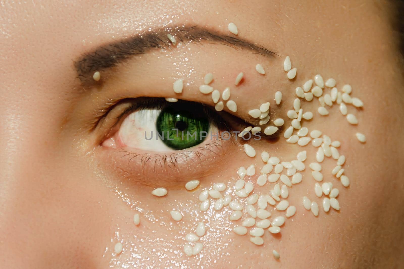 Open, green eye of a woman with white sesame seeds on the eyelid, around the eye. Expressive look