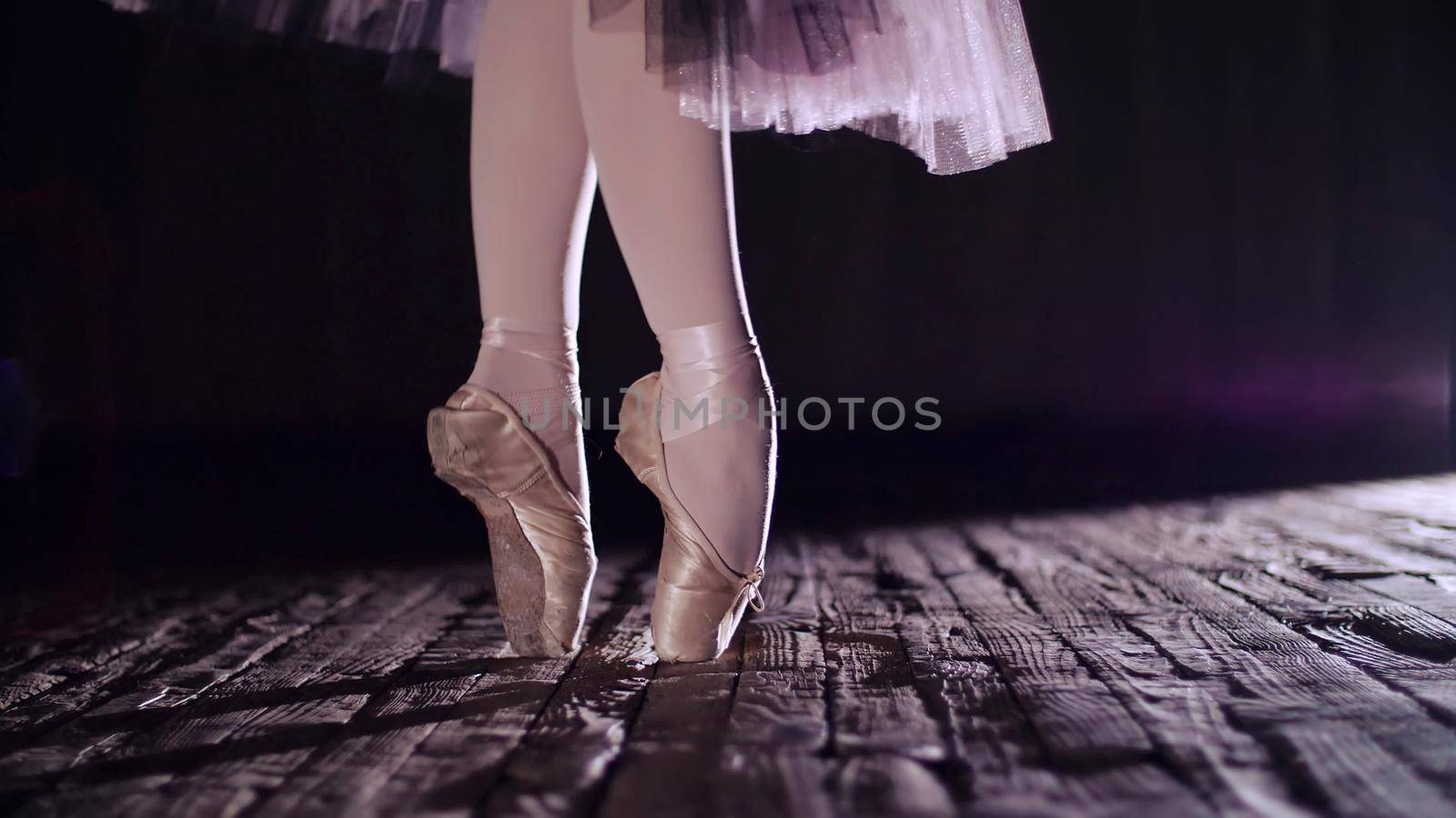 close up, in rays of spotlight, on stage of old theater hall. ballerina in white ballet skirt, raises on toes in pointe shoes, performs elegantly a certain ballet exercise, en tournaht suivi. High quality photo