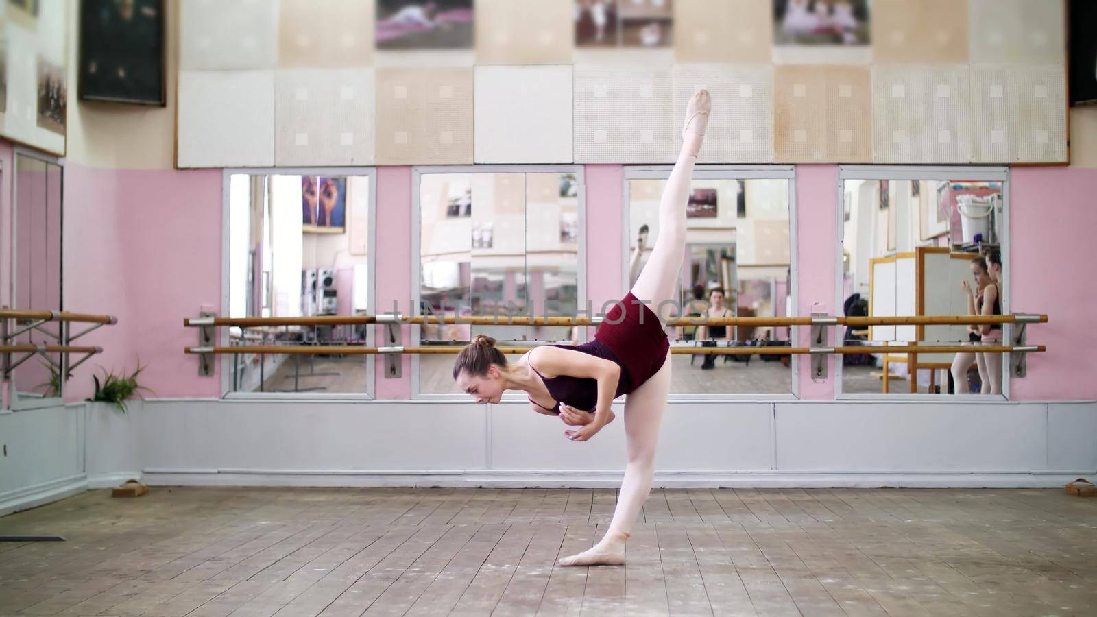 in dancing hall, Young ballerina in black leotard performs grand battement back, raises her leg up behind elegantly, in ballet class. High quality photo