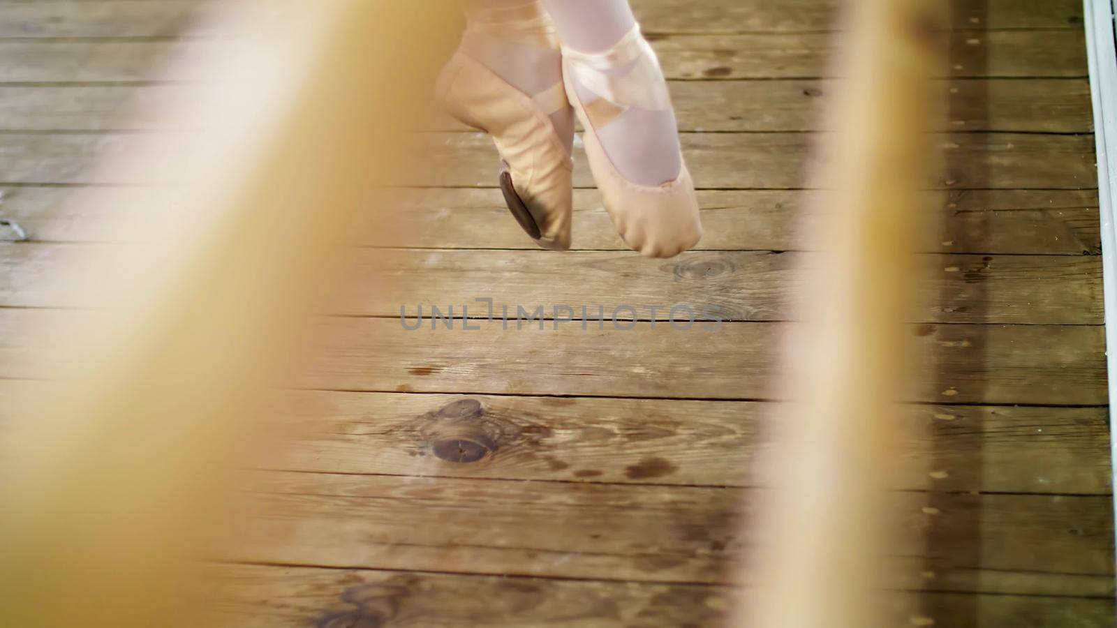 close up, in dancing hall, ballerina performs pas soute, jumping in ballet shoes near barre, on an old wooden floor, in ballet class. High quality photo
